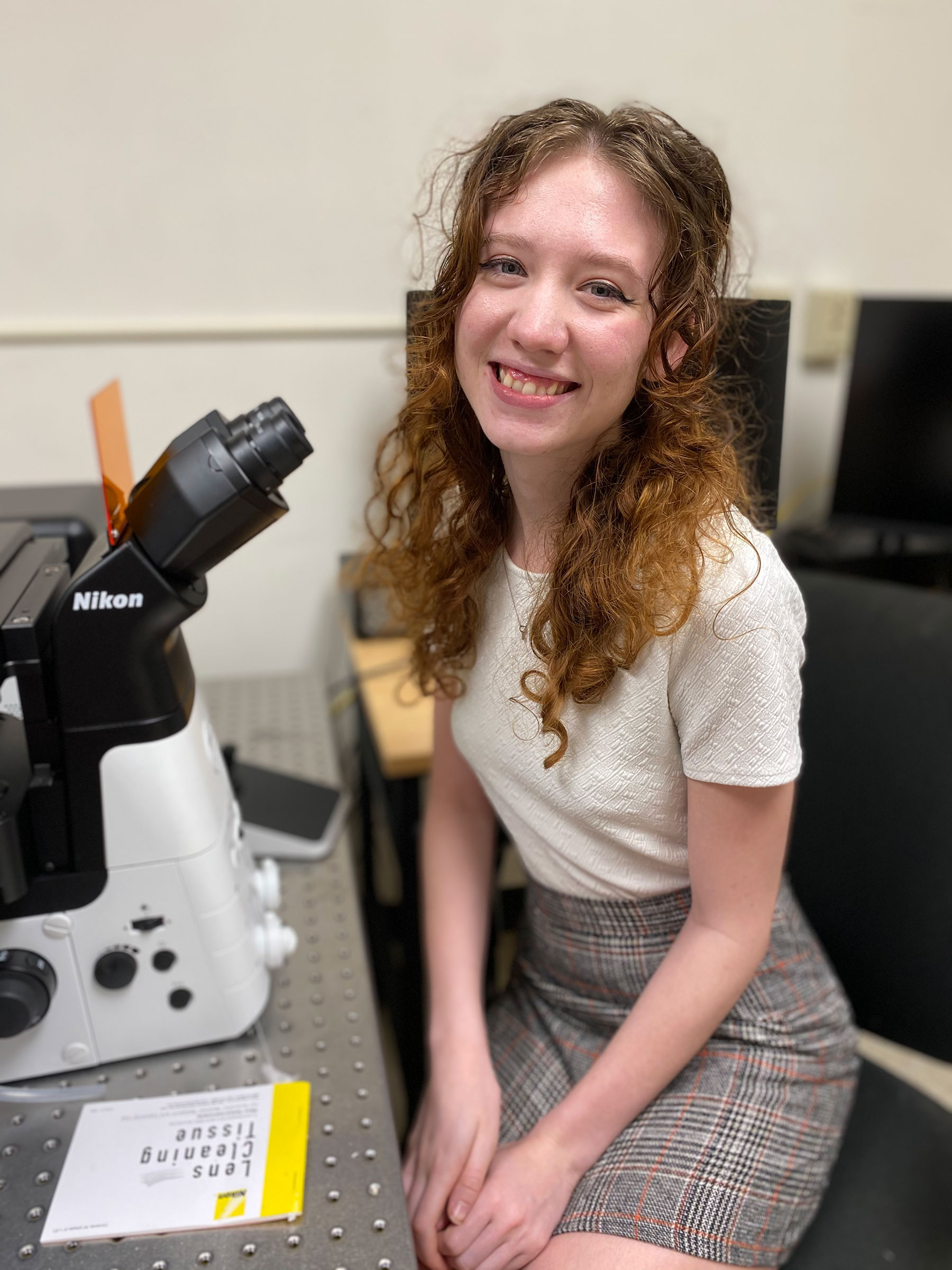 The student sits at the high-powered microscope in Sage Hall