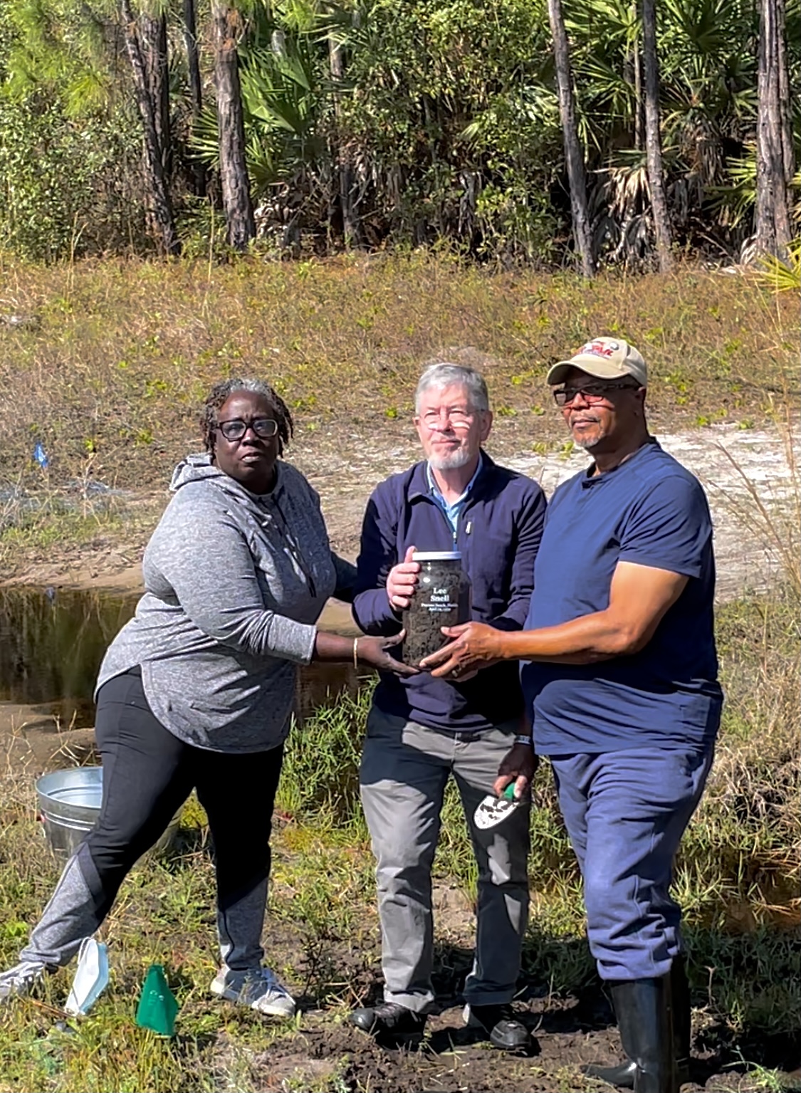 Three people hold a jar of soil collected from a lynching site outside Daytona Beach.