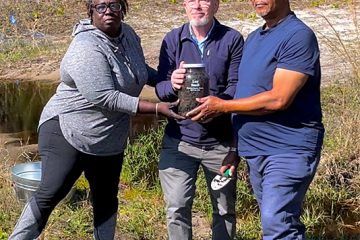 Three people hold a jar with soil collected from the site of a 1939 lynching outside Daytona Beach