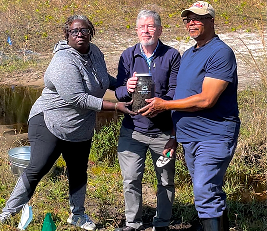 Three people hold a jar with soil collected from the site of a 1939 lynching outside Daytona Beach