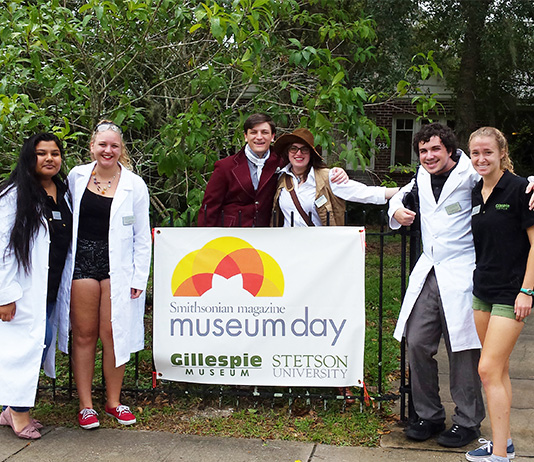 Six students stand in front of the museum with a sign