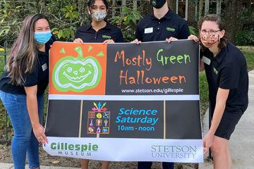 Four students hold a poster outside the Gillespie Museum for the event