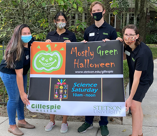 Four students hold a poster outside the Gillespie Museum for the event