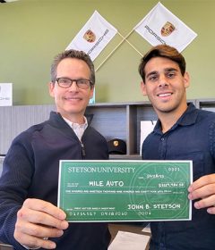 Two people stand holding a check