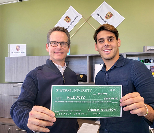 Two people stand holding a check