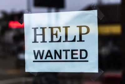A "Help Wanted" sign appears in a business window as record numbers of workers quit during the "Great Reassessment."