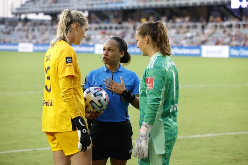 Natalie Simon talks to two soccer players on the field.