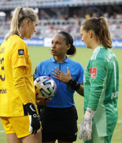 Natalie Simon talks to two soccer players on the field.