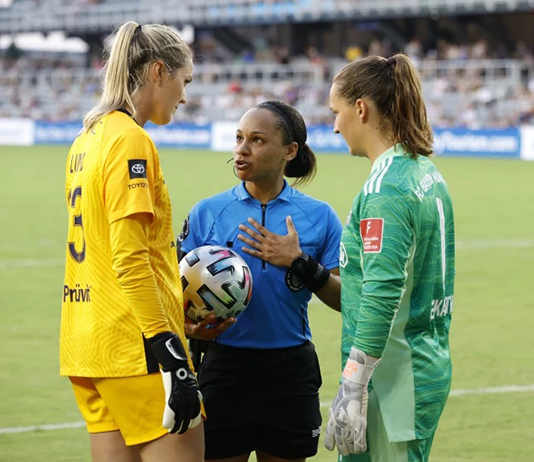 Natalie Simon talks to two soccer players on the field.