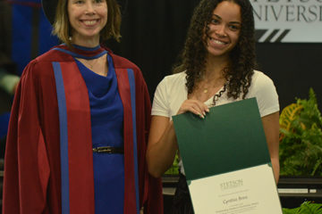 A student shows her award beside the College of Arts and Sciences Dean