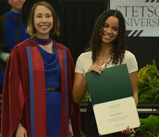 A student shows her award beside the College of Arts and Sciences Dean