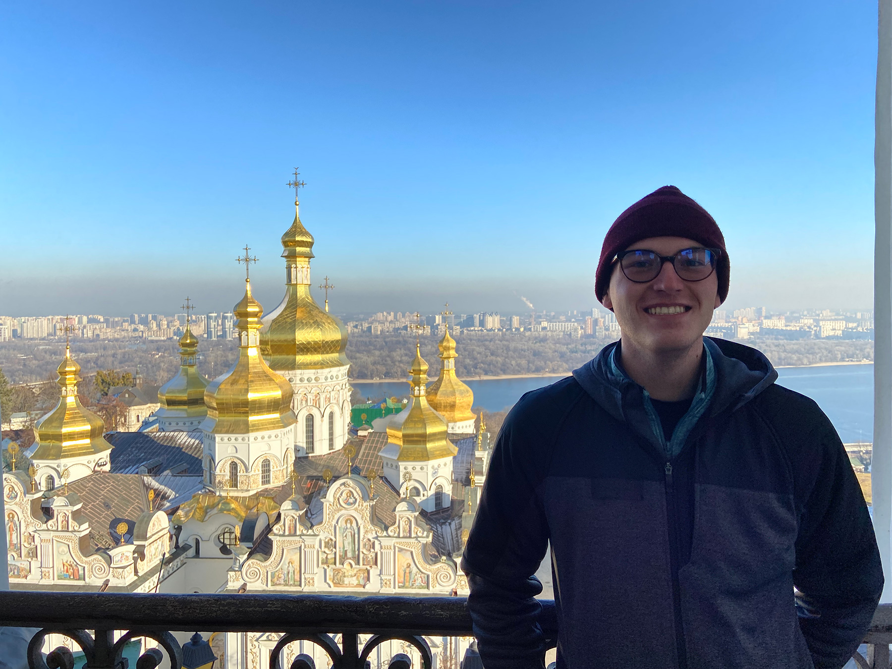 Jonah Helwig ’22 poses on a balcony in Ukraine with a pretty church behind him.