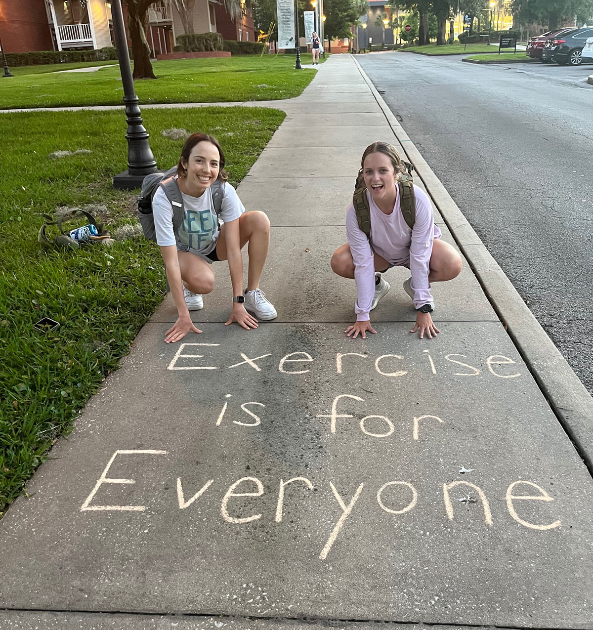 Two students pose beside a positive message, "Exercise is for Everyone," on the Hatter Track walking path.