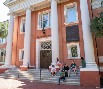 Students sit on the front steps of a historic academic building.