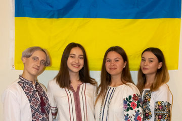 Four Ukrainian students stand in front of their country's flag.