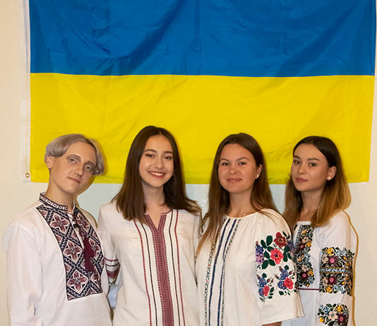 Four Ukrainian students stand in front of their country's flag.