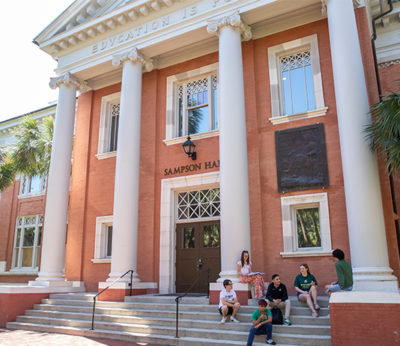 Students sit on the steps of a brick academic building