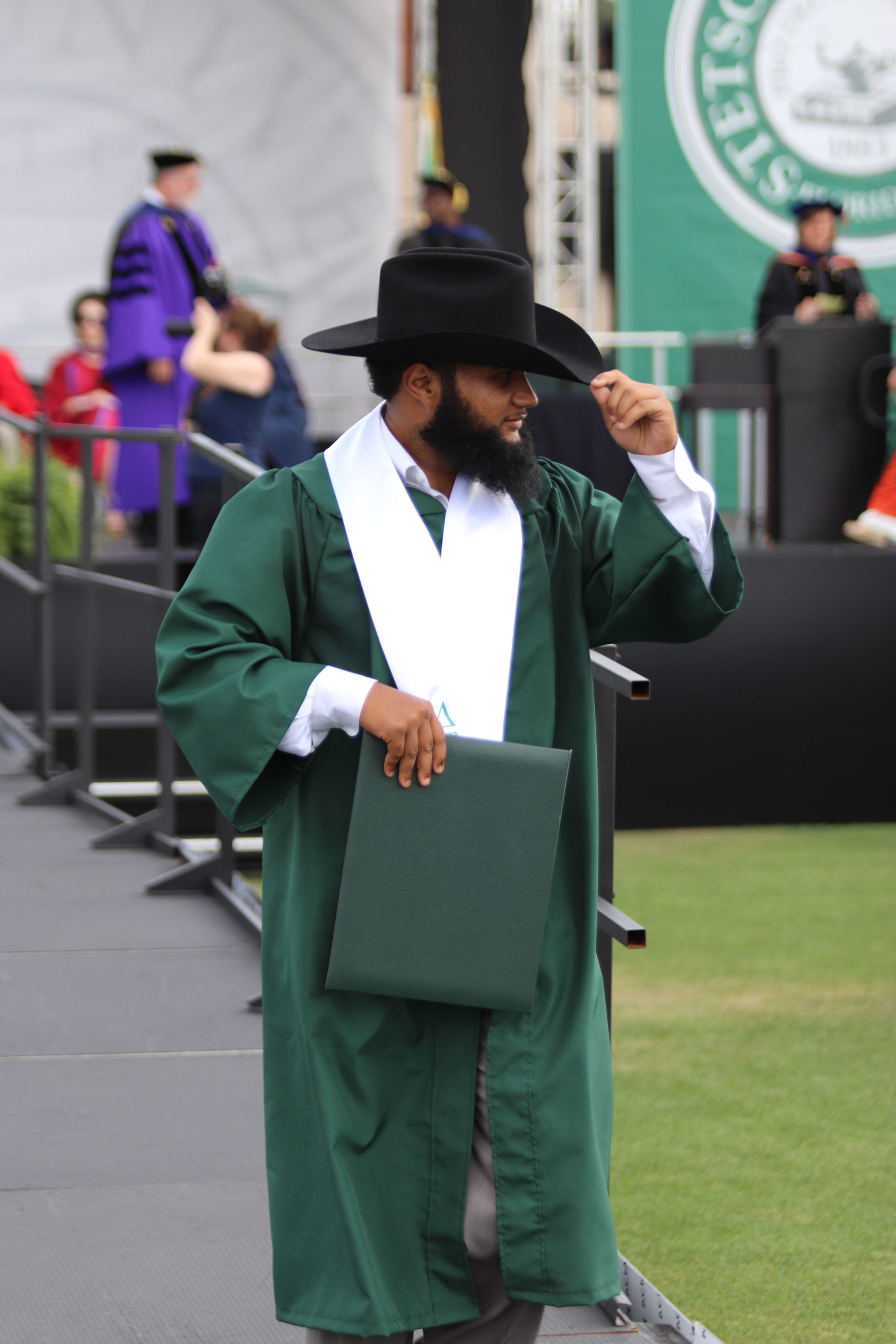 A graduate at Commencement wears a Stetson hat,.
