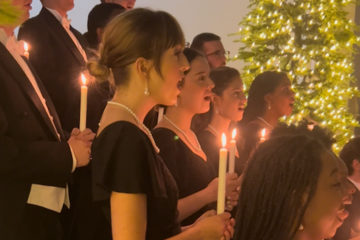 Students sing in a choir by candlelight with a Christmas tree in the background