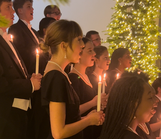 Students sing in a choir by candlelight with a Christmas tree in the background