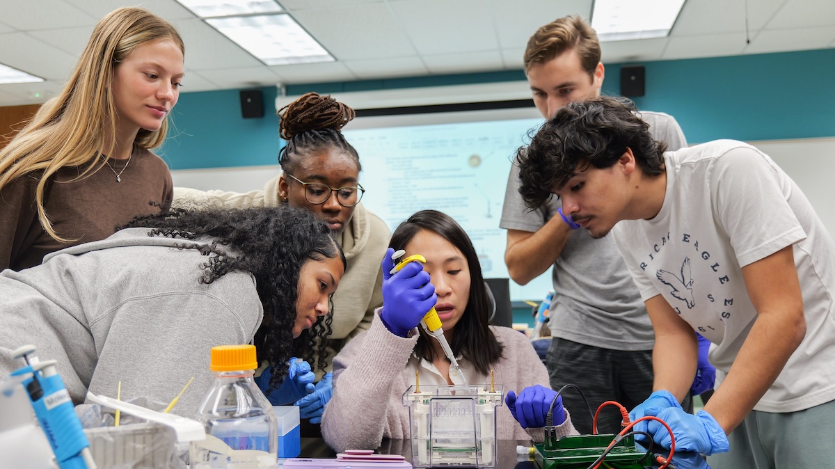 A professor works with students in a science lab.