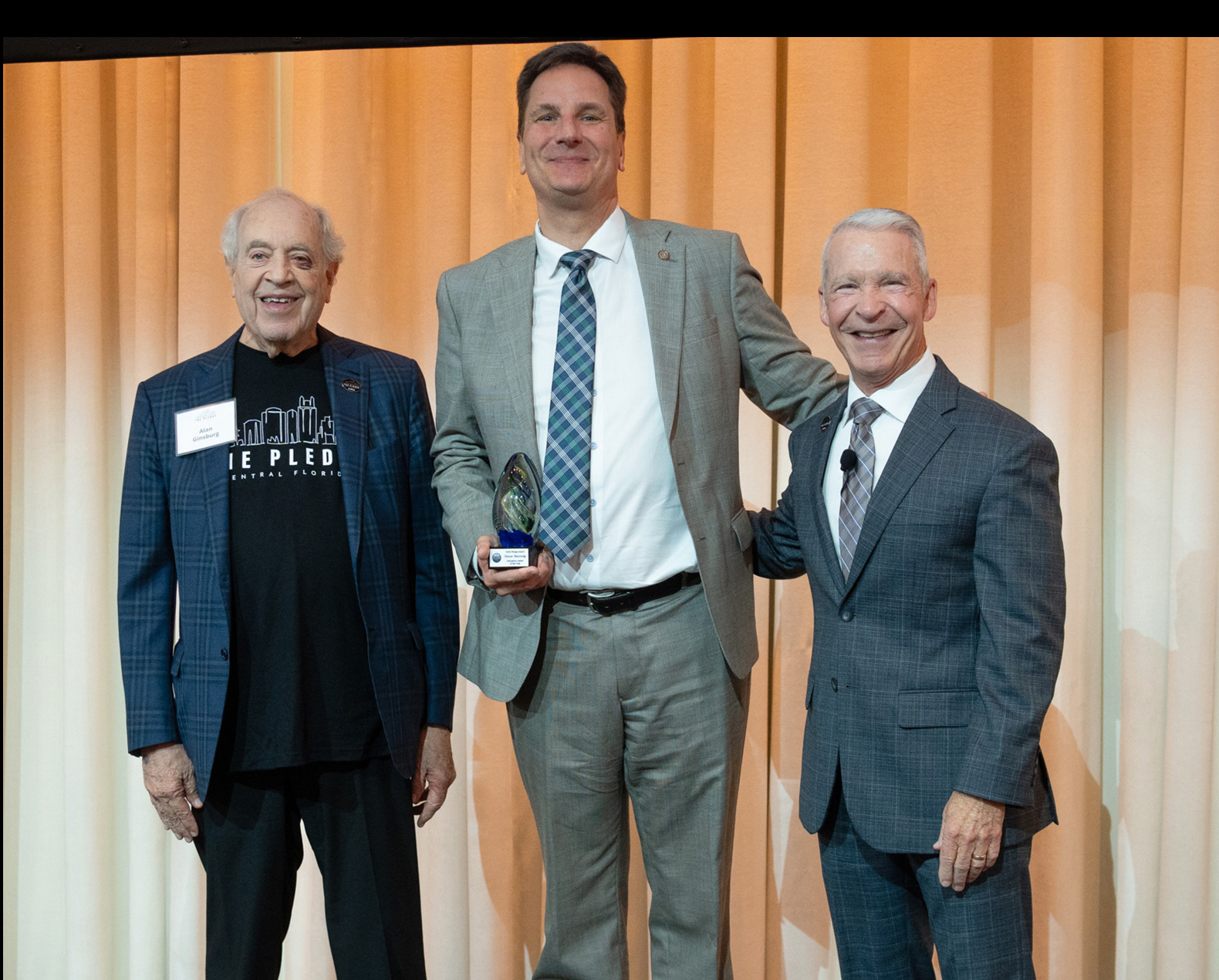 Three men stand on stage and one holds an award.