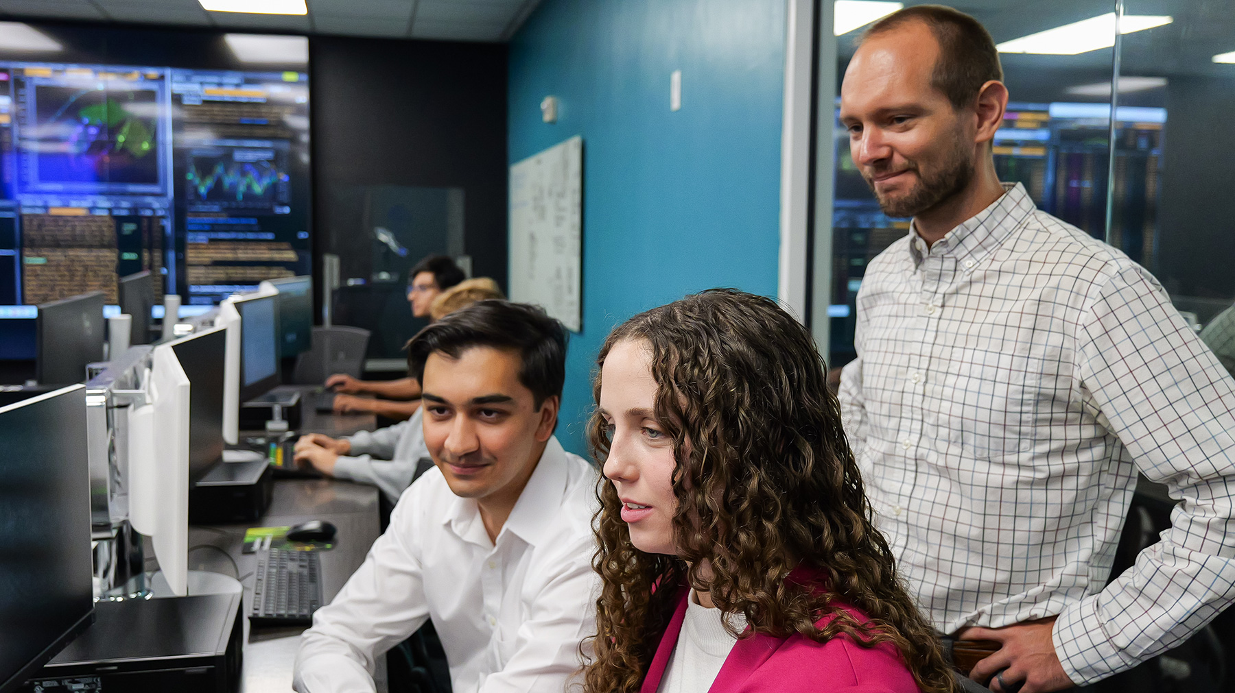 Students work at a computer with a professor behind them.