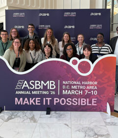 A group of people pose for a photo behind a banner that says ASBMB.