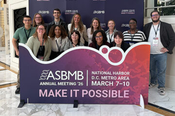 A group of people pose for a photo behind a banner that says ASBMB.