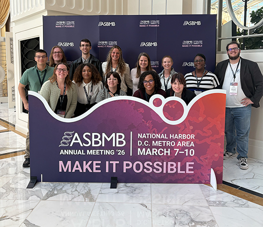 A group of people pose for a photo behind a banner that says ASBMB.