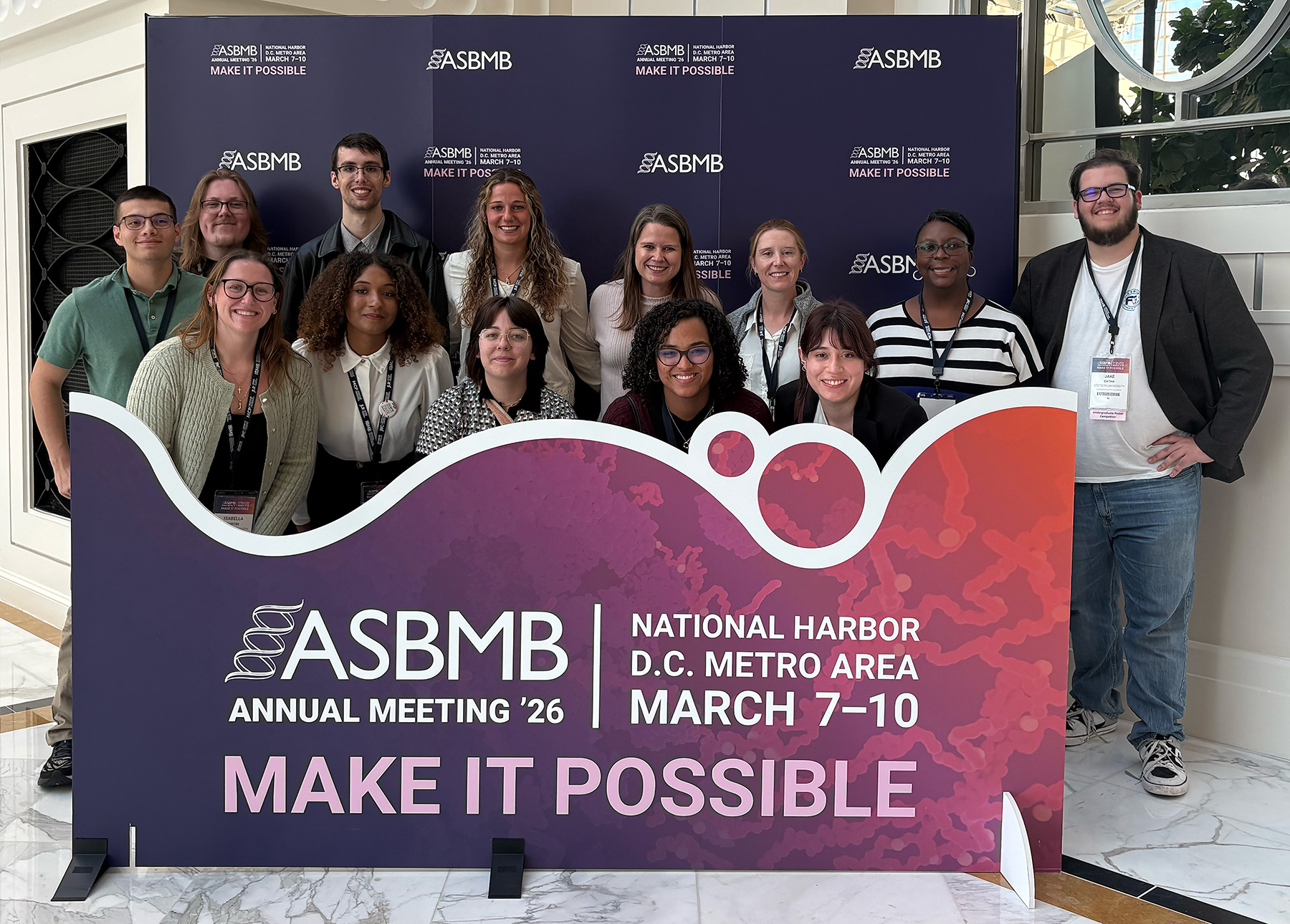 A group of people pose for a photo behind a banner that says ASBMB.