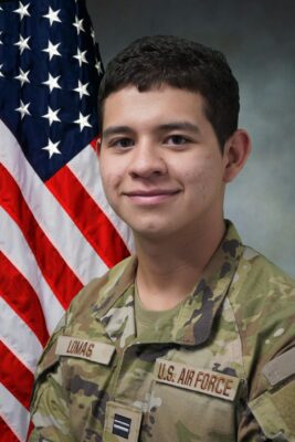 Portrait of a young man in military fatigues with a U.S. flag behind him.