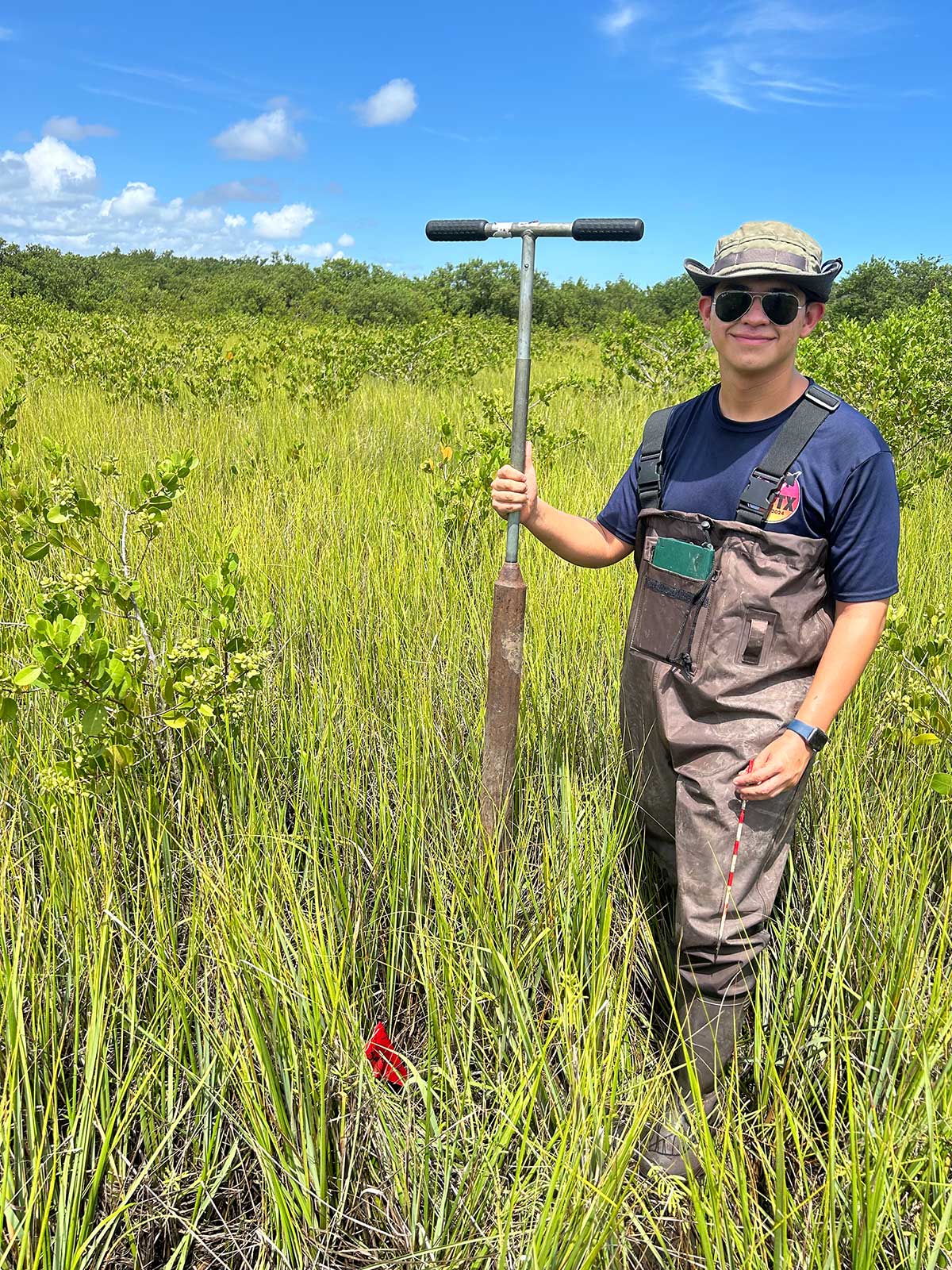 A young man stands in an open field with a piece of scientific equipment.