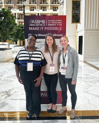 Three women pose by a ASBMB banner.
