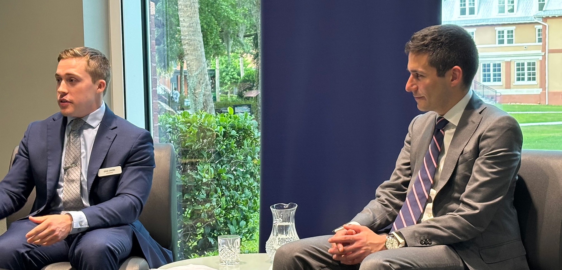 Two men dressed in suits sit side by side in discussion