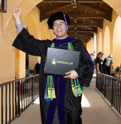 A man in a graduation cap and gown holds a diploma that says Stetson Law