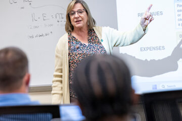 A female professor talks at the front of a classroom