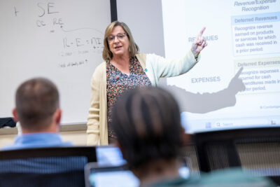 A female professor talks at the front of a classroom