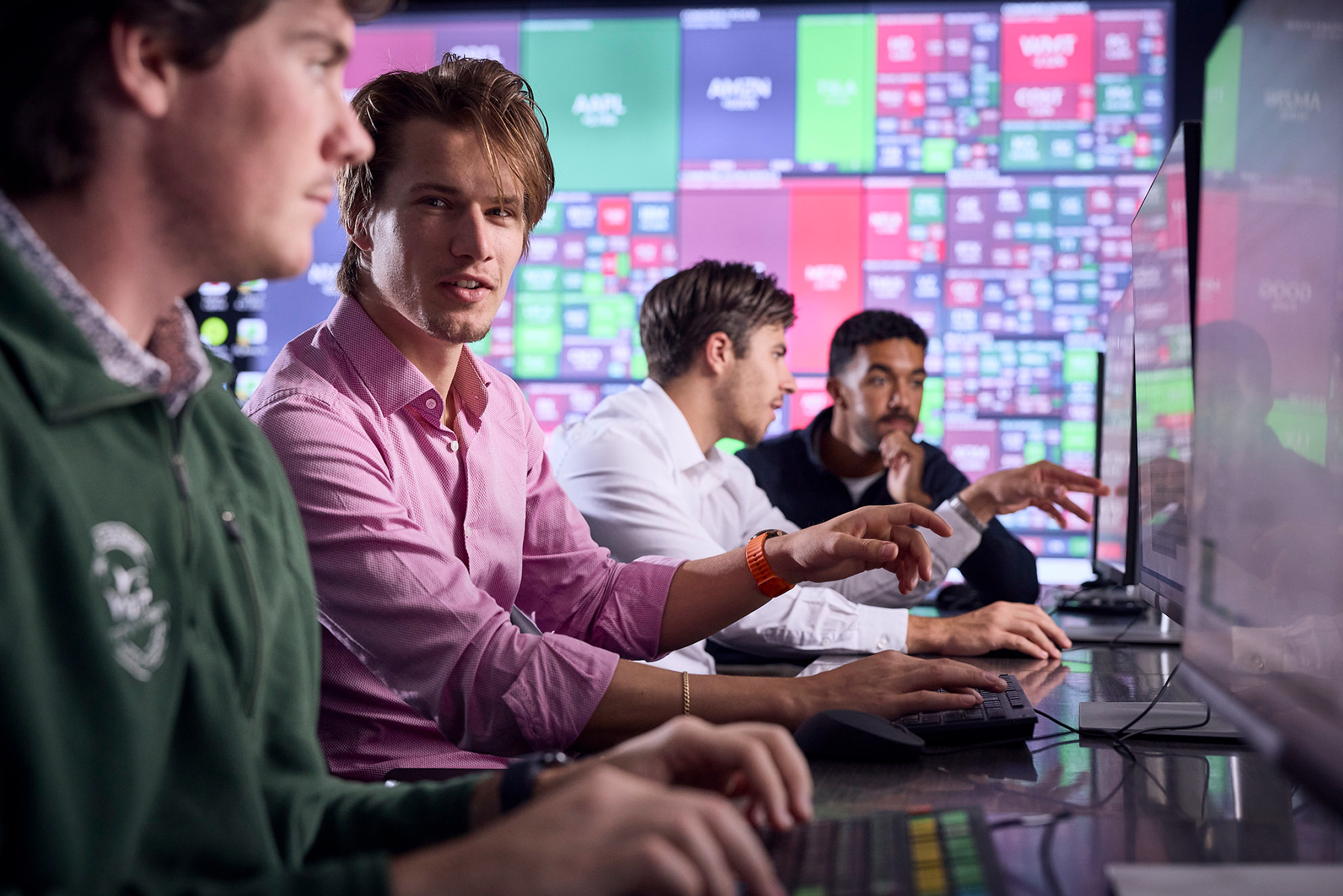 Students work at computers with a colorful screen behind them.