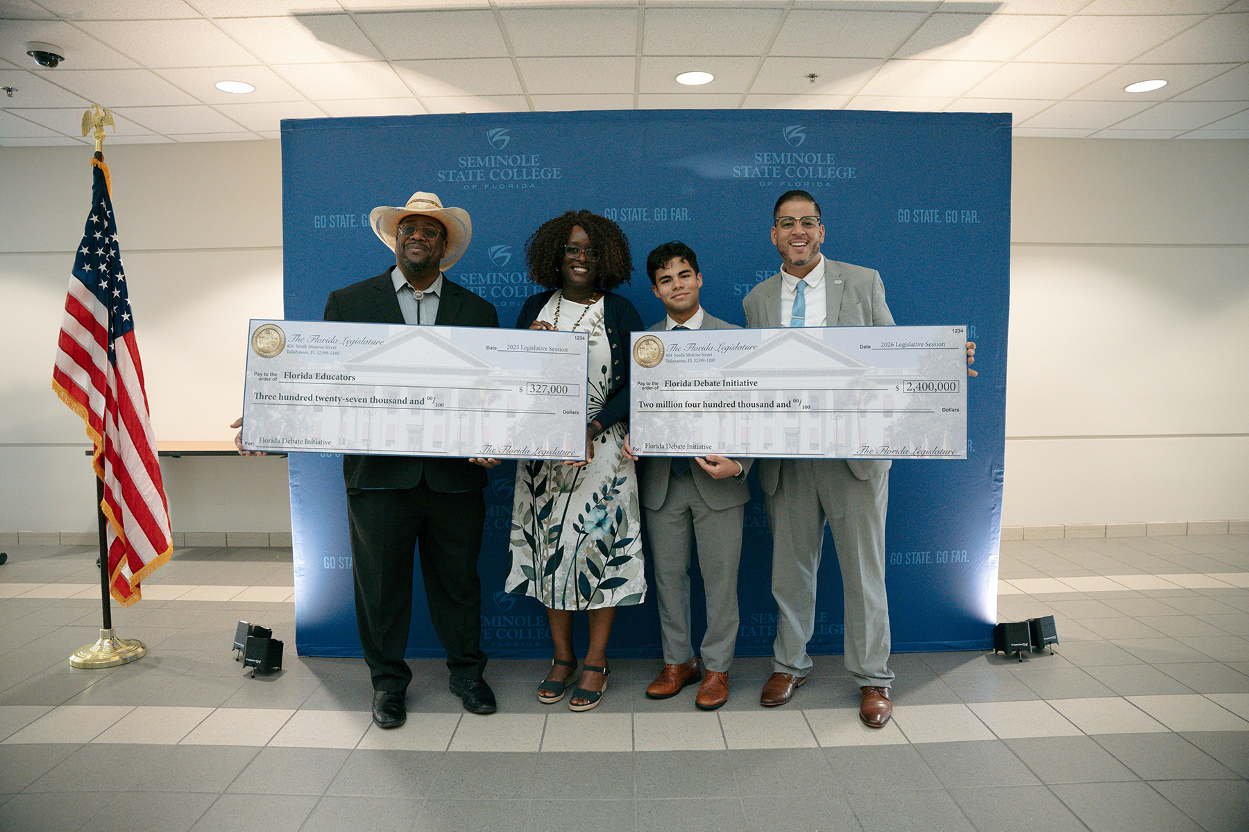 Four people in front of a blue background holding ceremonial checks