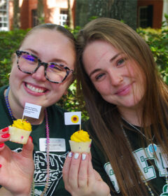 Two students each holding a mini cupcake with yellow icing