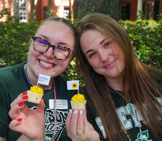 Two students each holding a mini cupcake with yellow icing